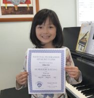 Here's an alt tag for the image: Smiling girl holding piano achievement certificate.