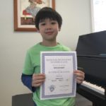 Here's a short alt tag for the image: Smiling boy holding music achievement certificate.